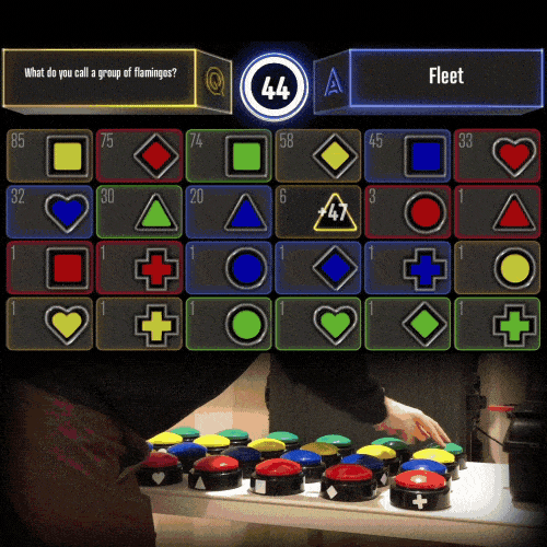 Rows of dome buzzers on a table, a hand hitting one, and the 24-tile trivia board counting down